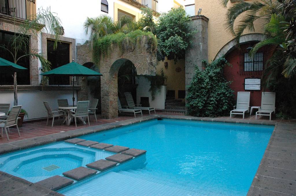 Blue cool swimming pool and jacuzzi, half arch, volcanic stone, tile, bushes, patio furniture, plastic owl, Hotel De Mendoza, Guadalajara, Jalisco, Mexico